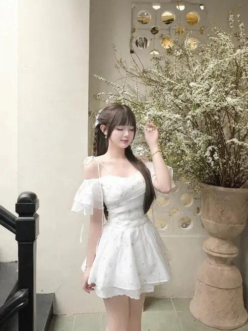 Cô gái mặc đầm trắng tay bồng đứng bên lan can gỗ, nắng chiều hắt nhẹ lên tóc và gương mặt mỉm cười