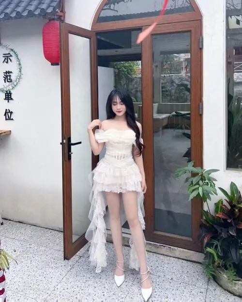 Cô nàng váy trắng hai dây tạo dáng cạnh hồ nước, làn gió nhẹ làm tóc bay và khung hình trông rất mát