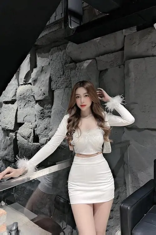 Sắc trắng tinh khôi của chiếc váy xòe làm cô gái nổi bật giữa nền kính sáng, tay cầm túi nhỏ đầy duyên