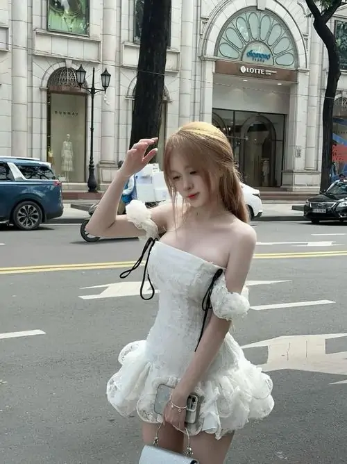 Gái xinh mặc váy trắng ngắn bước nhẹ trên lối lát đá, tóc buộc nửa đầu và nụ cười nhìn sang rất tươi
