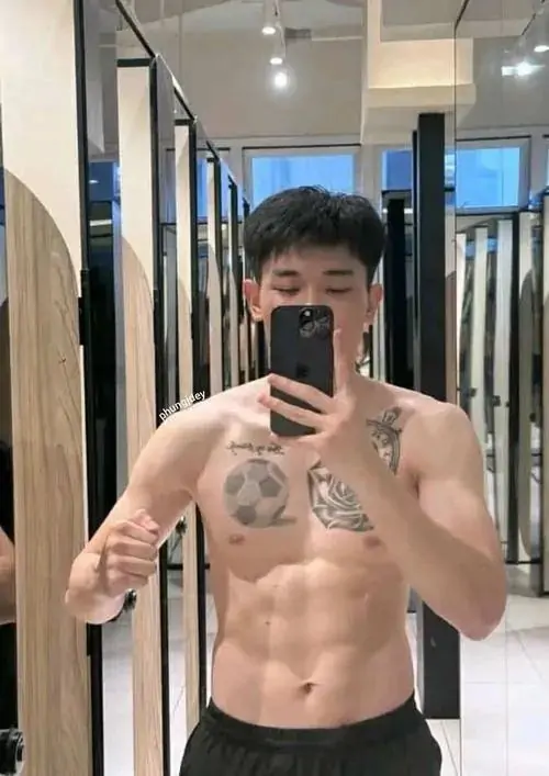 Selfie trong phòng thay đồ cho thấy chàng trai đeo kính, thân trên trần, quần sáng màu, hình xăm nhỏ và cơ bụng gọn