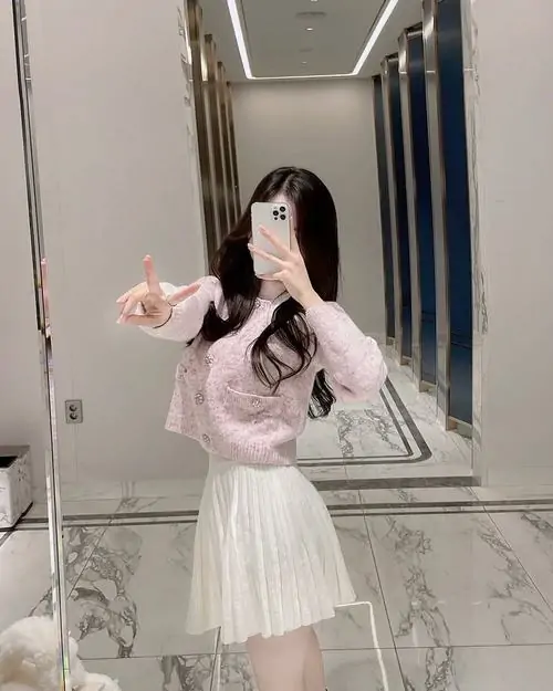 Góc phòng sang màu kem làm mỹ nữ tạo dáng mềm mại nổi bật, váy trắng nhiều lớp và áo khoác hồng tạo nét nữ tính
