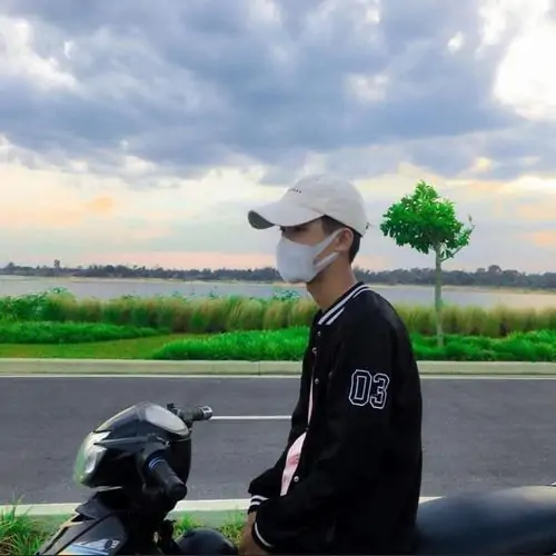 Dưới ánh nắng sân bóng, cậu bạn tuổi teen mặc áo thể thao trắng cười nhẹ, mái tóc đen bồng tạo vẻ năng động dễ gần