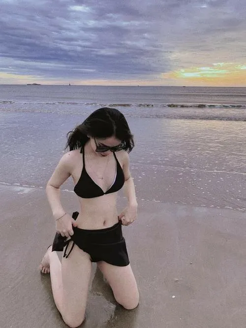 Ảnh gái xinh mặc bikini 2 mảnh nhỏ màu đỏ đứng giữa làn nước trong, phía sau là đá núi và bầu trời xanh rực