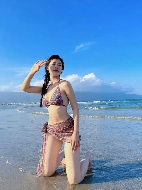 Tông đen trắng trên bãi cát tạo nét cổ điển, người mẫu đội mũ rộng vành mặc bikini đen với dáng ngồi mềm mại