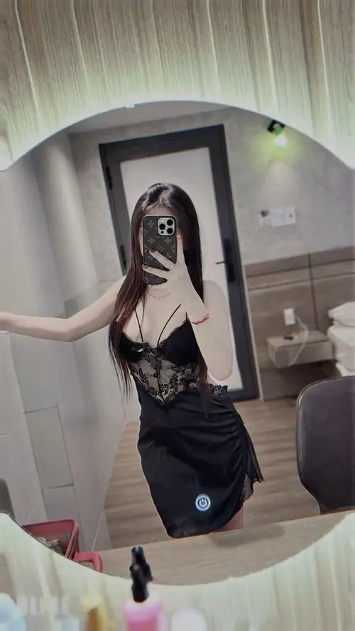 Trong căn phòng tông kem, cô gái mặc váy ngủ đen đứng trước gương, dáng người thanh mảnh cùng biểu cảm kín đáo