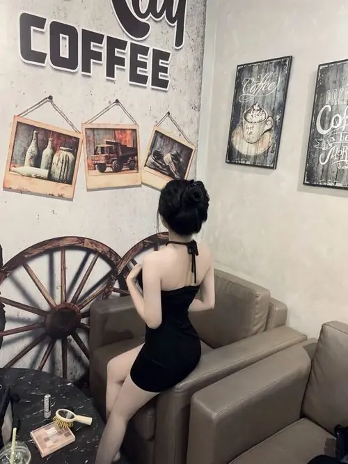 Trong phòng khách ấm áp, ảnh mỹ nhân phối đồ với váy ngắn đen có tay áo voan, mái tóc dài và dáng đứng duyên