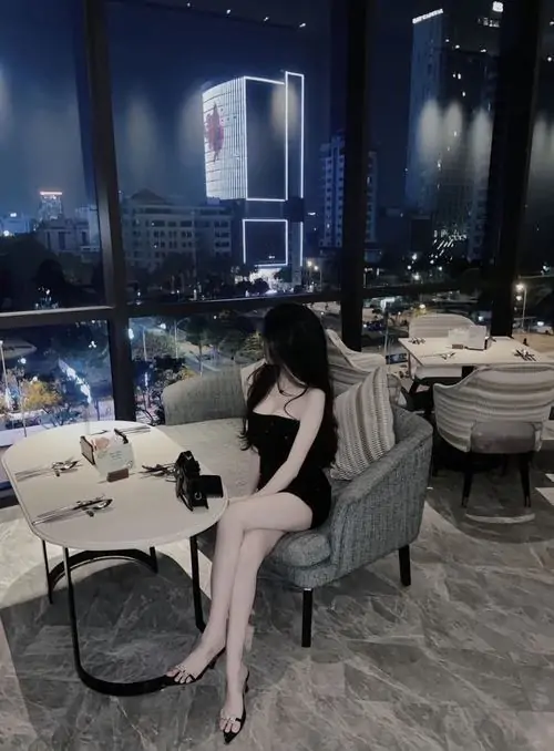 Cô nàng ngồi quay lưng trước tường trang trí cà phê, váy đen ôm sát và kiểu tóc ngắn tạo vẻ gọn gàng