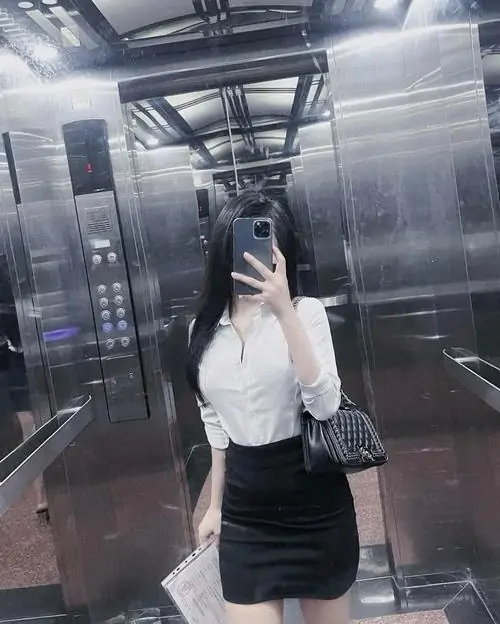 Trước khung cảnh nhà hàng đêm, cô gái mặc váy đen ngồi trên ghế, ánh đèn thành phố phản chiếu sau lưng