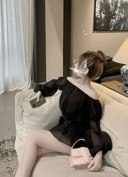 Cô nàng ngồi trên sofa trắng với ảnh thiếu nữ mặc váy đen dáng ngắn, tóc búi cao và ánh mắt nghiêng dịu dàng