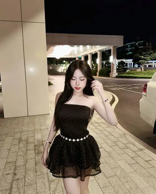 Không gian sân tối làm hình ảnh hot girl đầm đen ngắn thêm nổi bật, cô nàng đứng thẳng với túi xích và tóc xoăn nhẹ