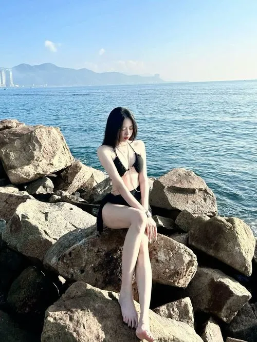 Tông màu nhạt bên hàng cọ tạo nét dịu, cô gái mặc bikini đen quay lưng nhẹ với mái tóc nâu và vai thon