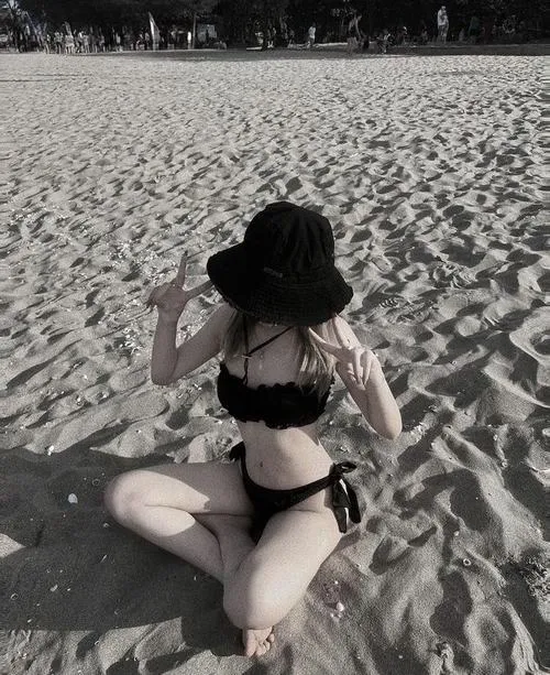Cô gái mặc bikini hồng nhạt đứng cạnh vách đá biển, tay đặt nhẹ bên hông và dáng người thon tạo nét duyên dáng