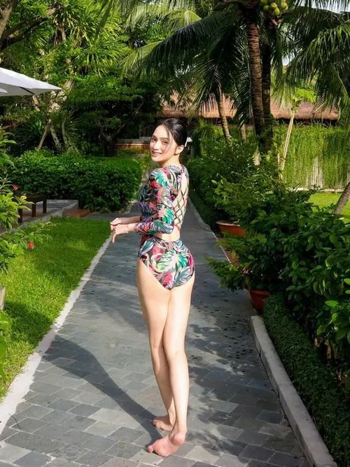 Giữa lối đi resort xanh mát, Hương Giang nghiêng dáng trong áo tắm họa tiết, tóc búi gọn và nụ cười nhẹ nhàng rất duyên