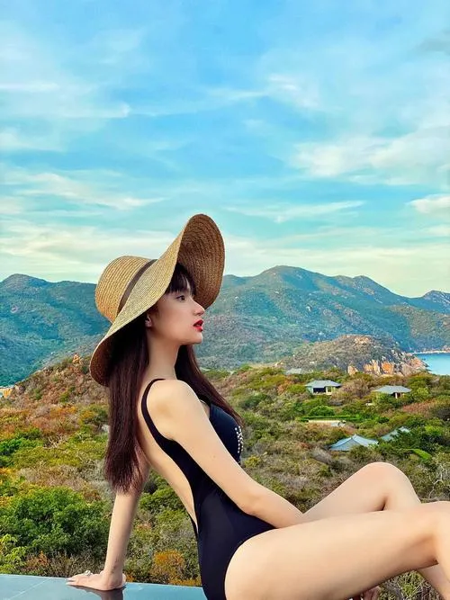 Trên triền núi nắng đẹp, hình nền Hương Giang quyến rũ cho thấy dáng ngồi thư thái, mũ rộng vành và áo tắm đen thanh lịch