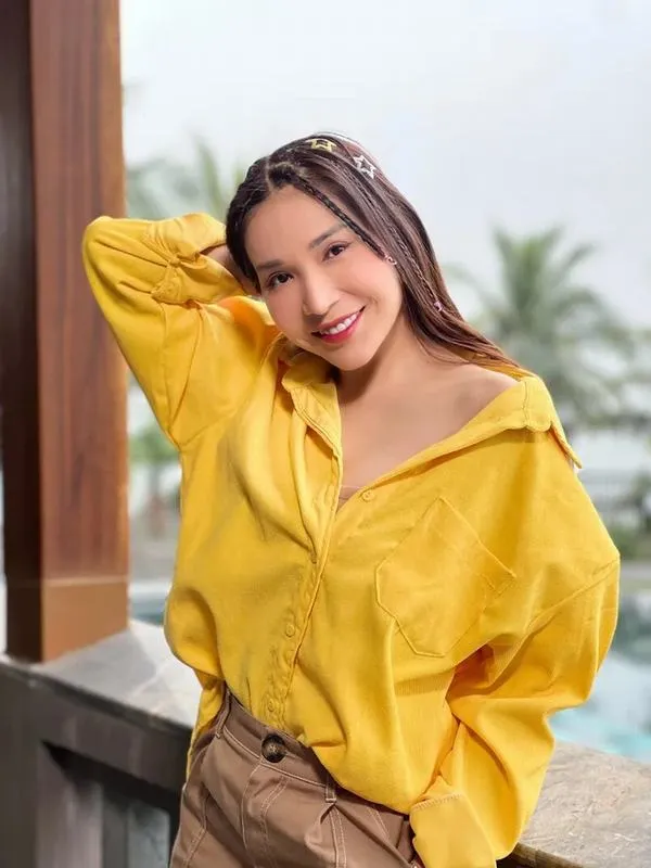 Sắc vàng của áo sơ mi rộng làm bức hình sáng hơn, cô gái mỉm cười tự nhiên bên hiên nhà với mái tóc buông ướt nhẹ
