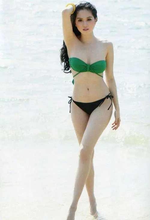 Bikini xanh lá trên nền biển trắng sáng tôn vòng eo thon, dáng bước nhẹ và mái tóc dài tạo cảm giác mùa hè rõ rệt