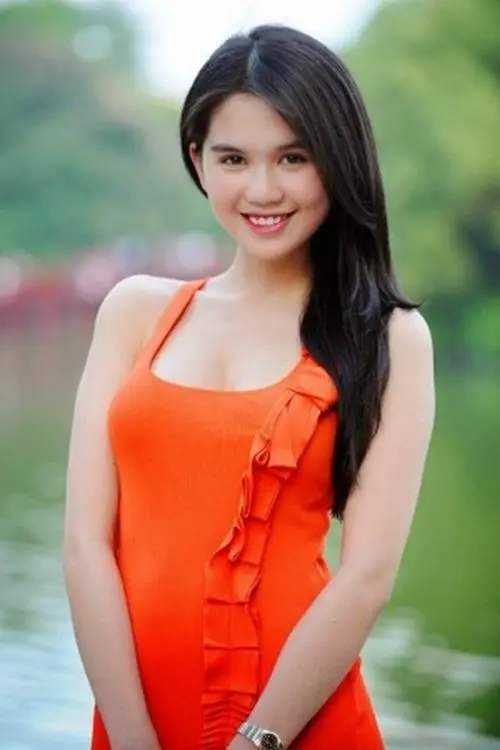 Bộ áo tắm cam nổi bật trên nền cây xanh, cô gái mỉm cười nhẹ với mái tóc đen buông vai và dáng đứng tự nhiên