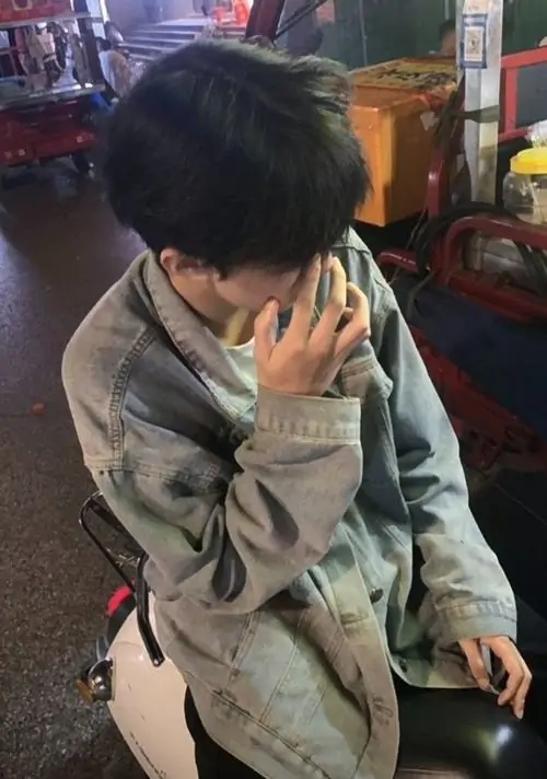 Bàn tay che kín hoàn toàn gương mặt của bạn nam tóc đen dày dặn mặc chiếc áo khoác cardigan len họa tiết thổ cẩm ấm áp.