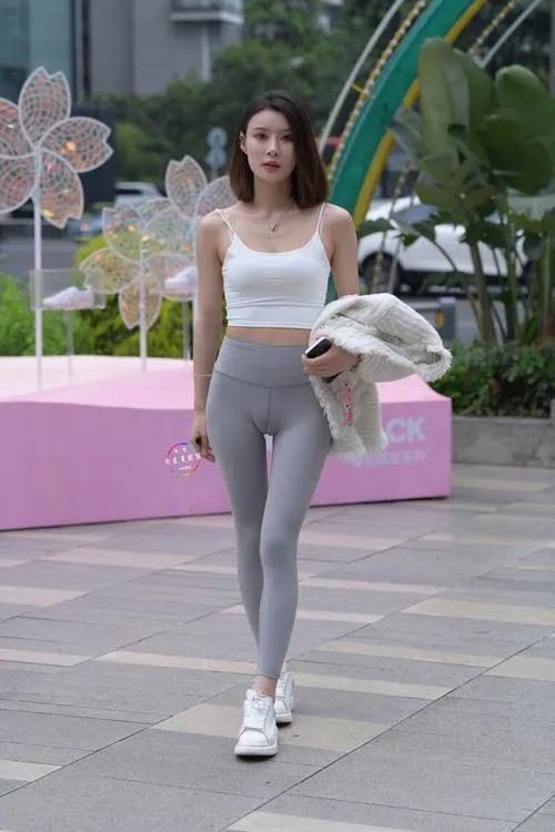 Giữa khuôn viên nhiều cây xanh, cô gái mặc áo trắng và legging xám ngồi trên ghế, dáng chụp thẳng tạo cảm giác trong trẻo