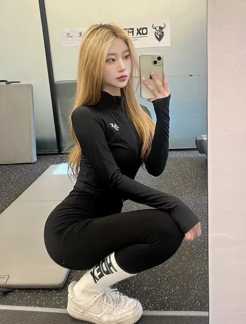 Cô gái tóc vàng chụp gương trong outfit đen ôm sát, dáng ngồi thấp giúp khoe cạp cao ôm eo và giày thể thao trắng