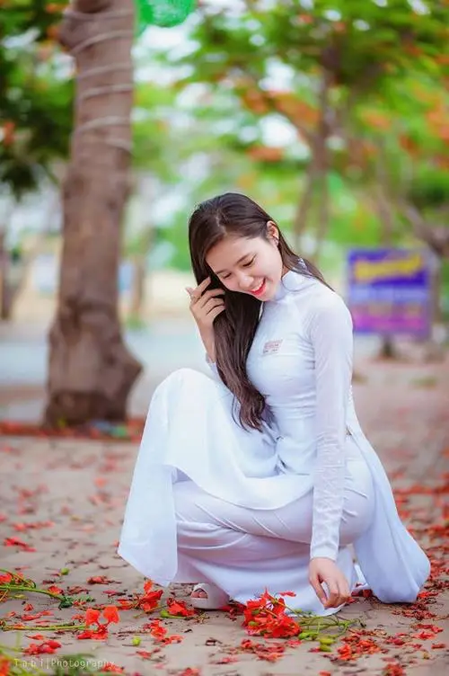 Trên thảm lá đỏ, cô gái áo dài xanh nhạt ngồi thấp ôm gối, tạo dáng chụp ảnh áo dài với nụ cười kín đáo