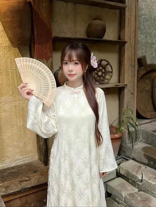 Áo dài trắng thêu nổi bật trong căn nhà gỗ cũ, cô gái cầm quạt nan che nhẹ mặt theo cách pose dáng áo dài e ấp