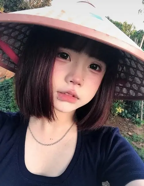 Chiếc nón lá và mái tóc ngắn khiến cô gái có vẻ mộc mạc, áo đen đơn giản nổi bật giữa nền cây xanh ngoài trời