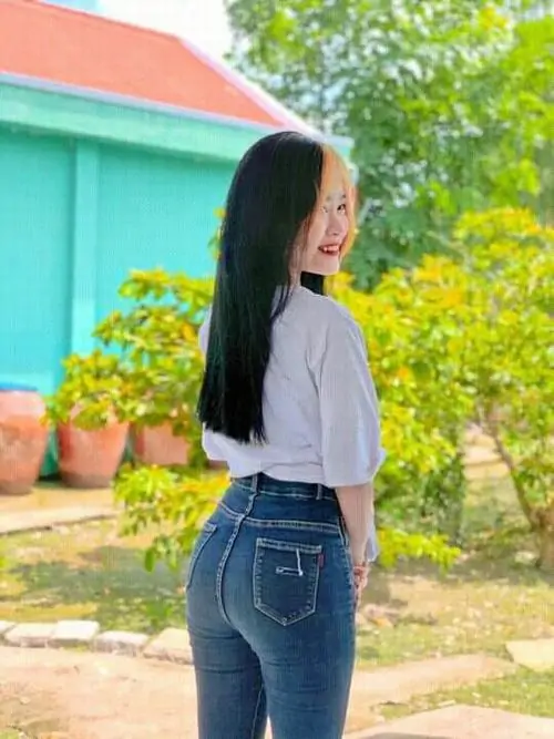 Nắng sân vườn phủ lên cô gái tóc dài áo trắng, quần jean xanh ôm dáng, cô quay nhẹ nhìn sang bên cạnh hàng cây xanh