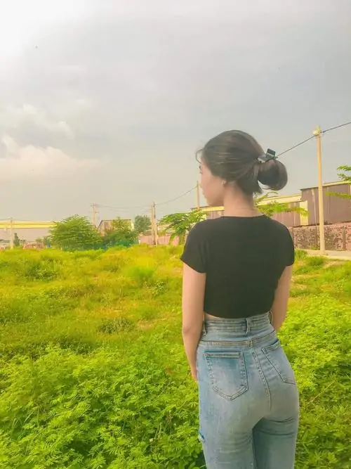Đồng cỏ vàng ven sông làm nền cho cô gái áo đen, jean xanh cạp cao, tóc búi gọn và dáng đứng yên bình