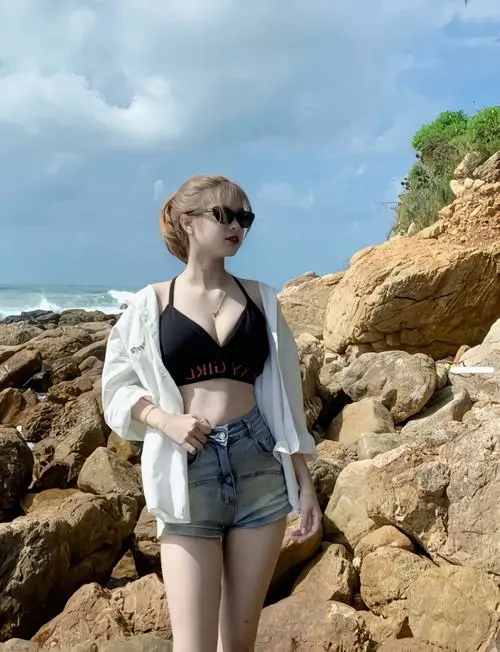 Trên bãi đá ven biển, hình ảnh người đẹp diện áo tắm đen kết hợp áo sơ mi trắng mở nhẹ tạo vẻ phóng khoáng và cuốn hút
