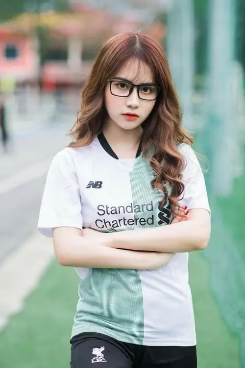Với kính gọng đen và áo Liverpool trắng xanh, ảnh mỹ nữ áo số đứng khoanh tay trên sân cỏ, thần thái tự tin