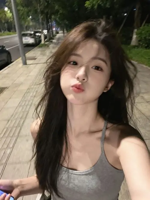 Trên vỉa hè nhiều cây, cô gái tóc dài mặc áo xám chụp selfie, môi chúm chím và ánh nắng tạo nét hình nền gái xinh xu hướng