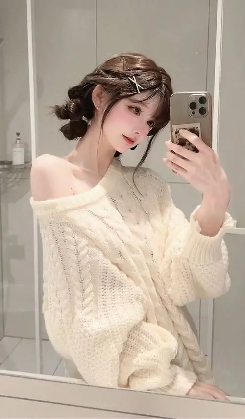 Cô gái chụp gương trong phòng với áo len trắng trễ vai, tóc uốn búi nhẹ và biểu cảm dịu dàng nhìn vào điện thoại