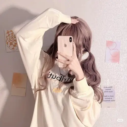 Áo hoodie sáng màu và điện thoại trước mặt tạo nên hình gái xinh giấu mặt, mái tóc nâu mềm cùng tông hồng trong phòng