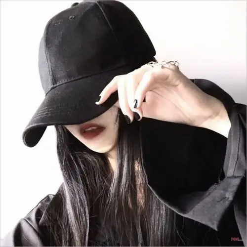 Mũ đen che nửa khuôn mặt, cô gái mặc áo đen dài tay, bàn tay đặt gần vành mũ tạo dáng sắc nét