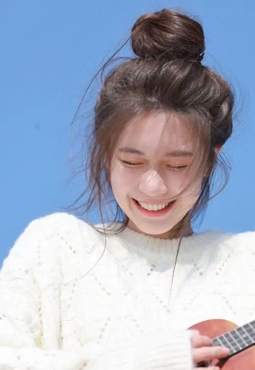 Dưới nền trời xanh trong, ảnh girl xinh cười mỉm mặc áo len trắng, tóc búi cao và hàng mi rủ tạo vẻ hồn nhiên