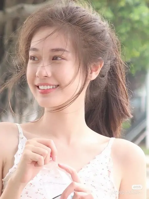 Giữa khung cảnh sân vườn, cô gái áo trắng ren tạo dáng tay nhỏ, nụ cười hiền và tóc buộc cao rất dịu mắt