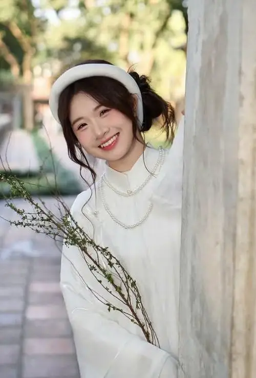 Tà áo lụa màu kem bay nhẹ trên lối gạch, cô gái xoay người chậm theo tạo kiểu với áo dài giữa chiều nắng