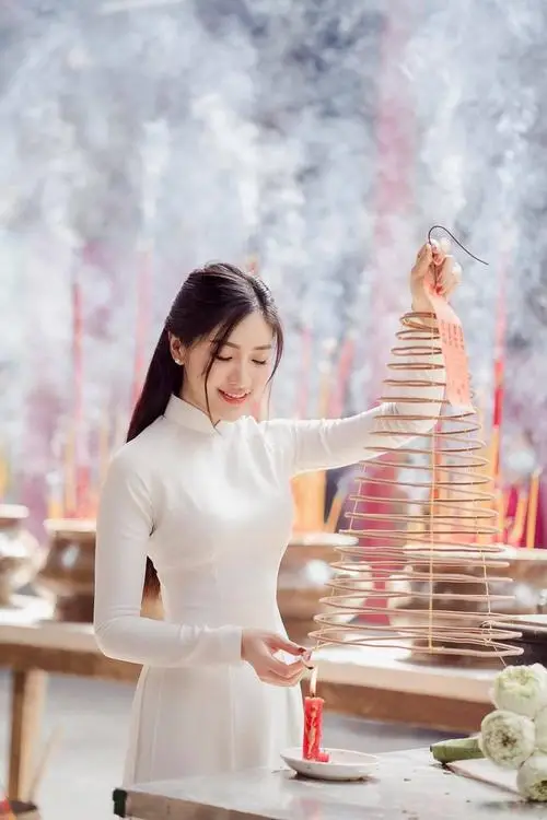 Cô gái áo dài xanh ngọc ngồi bên thềm chùa, hai tay đặt trên gối và mỉm cười hiền dưới mái ngói cũ