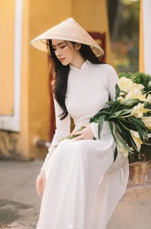 Bên bức tường rêu, cô gái áo dài đỏ đứng tựa vai, cổ áo cao và vòng ngọc trai làm nét mặt thêm sang
