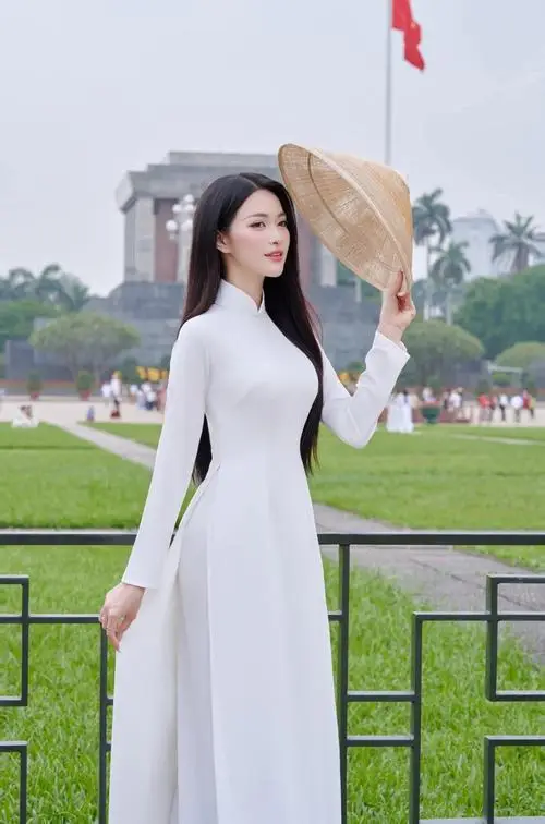 Người mẫu áo dài vàng bước qua sân gạch cổ, tạo dáng chụp ảnh áo dài cùng guốc mộc và mái tóc búi trễ