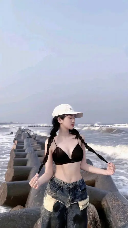 Bên ghế tắm nắng cạnh hồ bơi, cô gái kéo nhẹ khăn choàng qua eo, dáng đứng mềm và nụ cười kín đáo rất duyên