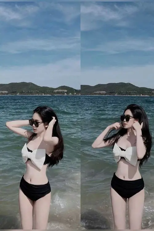 Hai cô gái đứng cạnh nhau gần biển trong bikini đen, cùng đưa tay chỉnh tóc và tạo dáng vui vẻ dưới bầu trời xanh