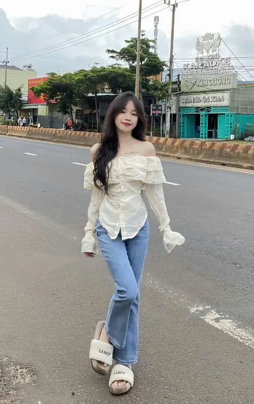 Bậc thang đá ngoài trời làm nổi bật cô gái mặc quần jean xanh, áo thun trắng, balo nhỏ và nụ cười rất tự nhiên