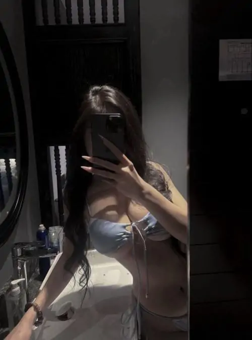 Áo choàng ngủ lụa màu ngọc trai phủ nhẹ trên vai, cô gái đứng cạnh rèm cửa trắng với mái tóc buông tự nhiên