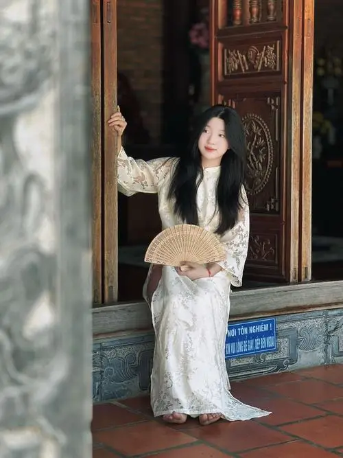 Cạnh ô cửa sổ tròn, nàng áo dài trắng cầm kiềng bạc trên tay, gợi cách đứng khi mặc áo dài rất đoan trang