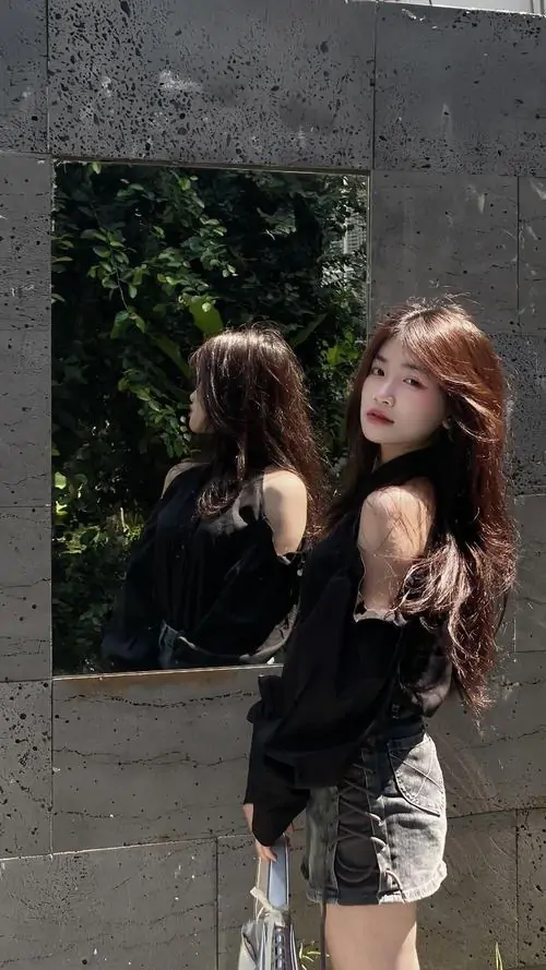 Hai cô gái trẻ diện outfit ngắn màu đỏ và trắng, đứng trước gương với dáng pose đồng bộ, tông ảnh hơi mờ kiểu hậu trường