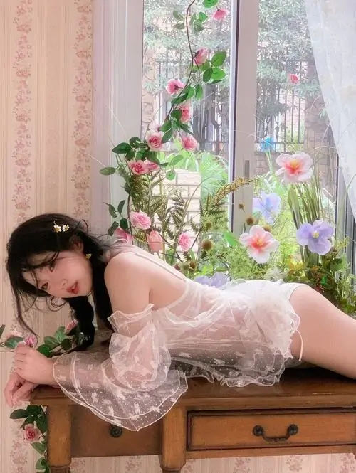 Bờ vai trần và dây áo thanh mảnh hiện nhẹ dưới áo choàng, cô gái nhìn về cửa sổ với thần thái thư giãn