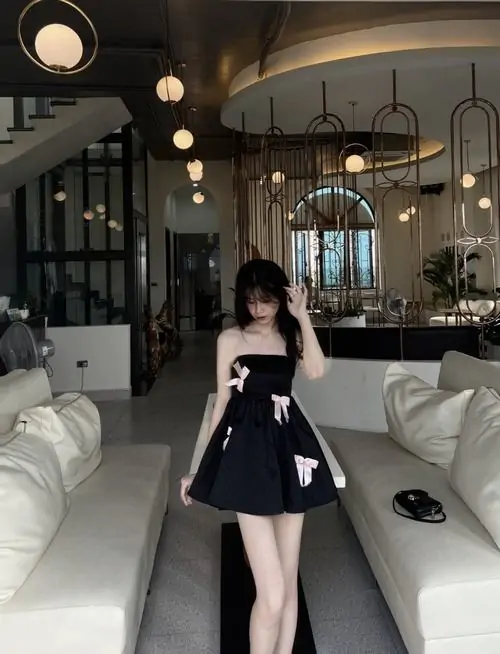 Một cô nàng tóc xoăn phối váy ngắn trên đầu gối cùng giày cao gót, dáng bước nhẹ trong bối cảnh phố tối giản